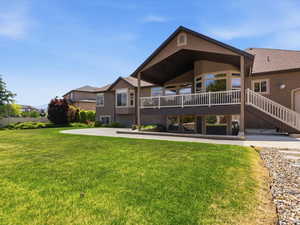 Expansive green lawn with a large rear patio, a multi-level deck featuring a white railing, and a covered upper outdoor area