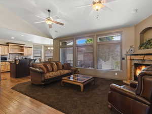 Living area featuring a stone surround fireplace with wood mantel, vaulted ceilings, and ceiling fans with light fixtures
