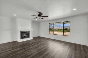 Unfurnished living room featuring a mountain view, ceiling fan, a warm lit fireplace, ornamental molding, and dark wood-style flooring