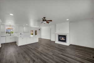 Unfurnished living room featuring a ceiling fan, a glass covered fireplace, dark wood-type flooring, and recessed lighting