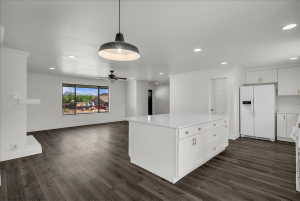 Kitchen with white refrigerator with ice dispenser, a kitchen island, crown molding, open floor plan, and decorative light fixtures