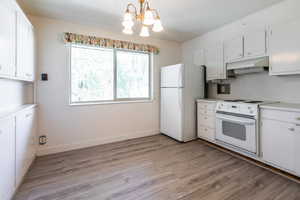Kitchen with white cabinets, light countertops, white appliances, and hanging lights