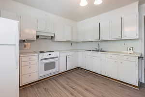 Kitchen featuring white appliances, light countertops, white cabinets, and light wood finished floors