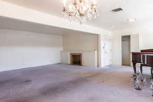 Unfurnished living room featuring carpet flooring, a fireplace with flush hearth, and hanging lights