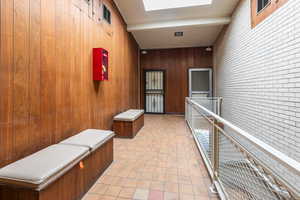 Corridor with wooden walls, light tile patterned flooring, and beamed ceiling