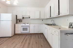 Kitchen with white appliances, light countertops, white cabinets, light wood finished floors, and a chandelier