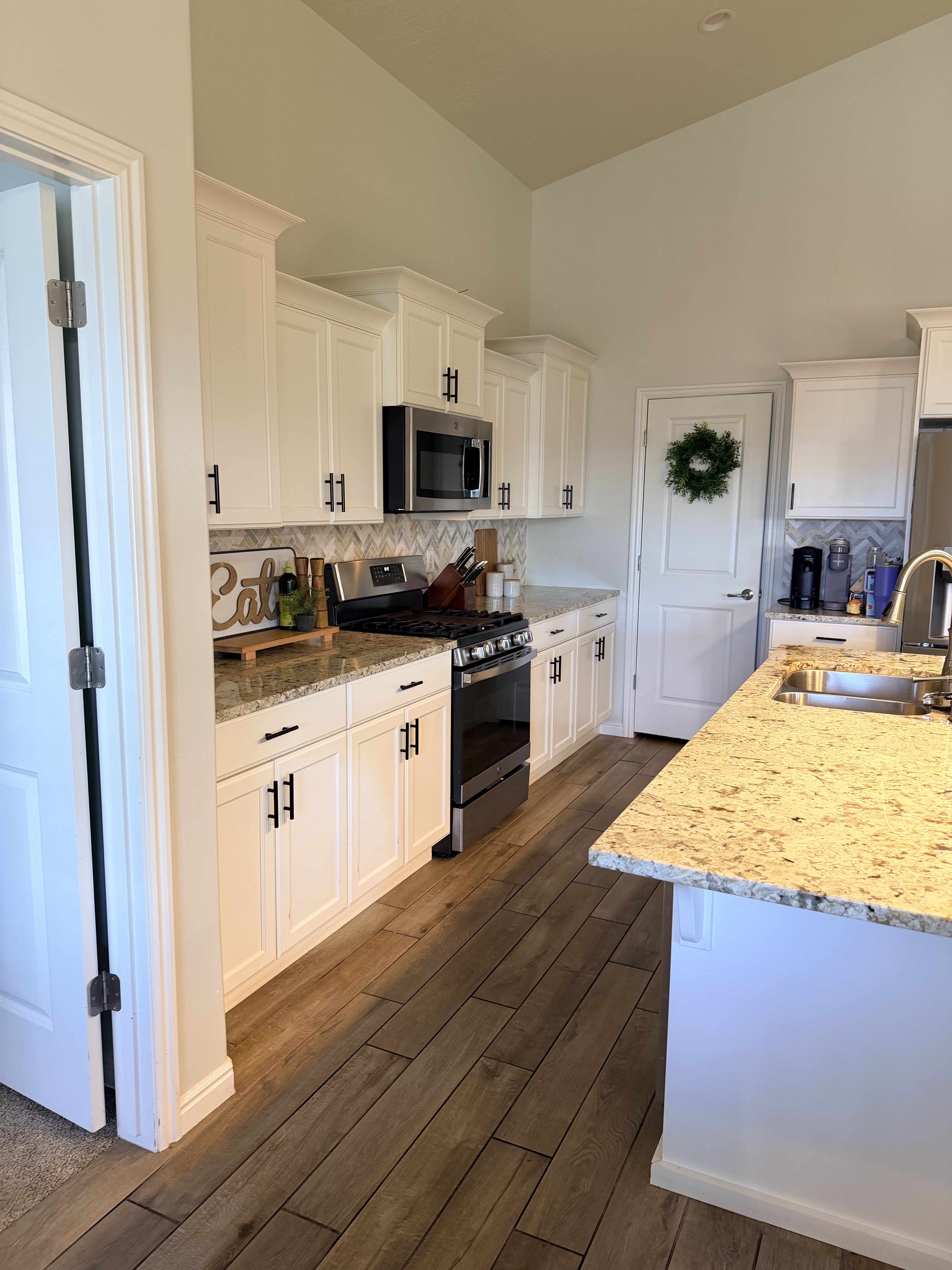 Kitchen featuring stainless steel appliances, white cabinets, light stone countertops, and vaulted ceiling