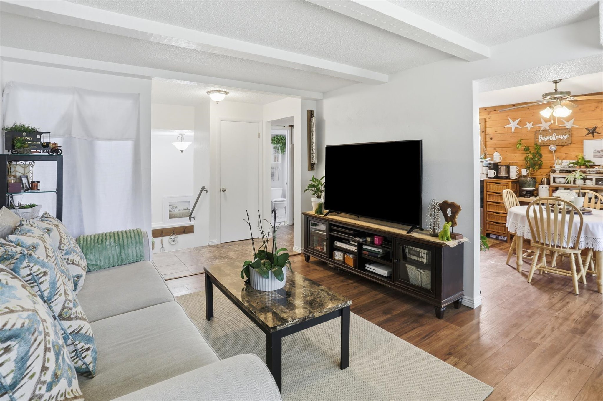 Living area with a textured ceiling, ceiling fan, beam ceiling, wooden walls, and wood finished floors