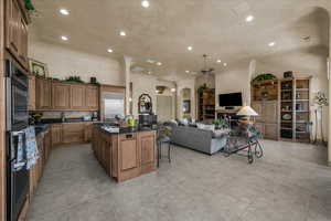 Kitchen featuring arched walkways, wood finish cabinets, open floor plan, dark stone countertops, and a breakfast bar area