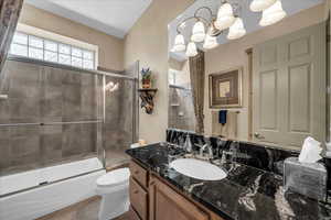 Full bathroom featuring vanity, healthy amount of natural light, shower / bath combination with glass door, and a chandelier