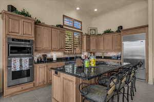 Kitchen with dark stone countertops, a kitchen bar, stainless steel appliances, a kitchen island, and wood finish cabinets