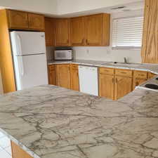 Kitchen with white appliances, wood finish cabinetry, and light countertops