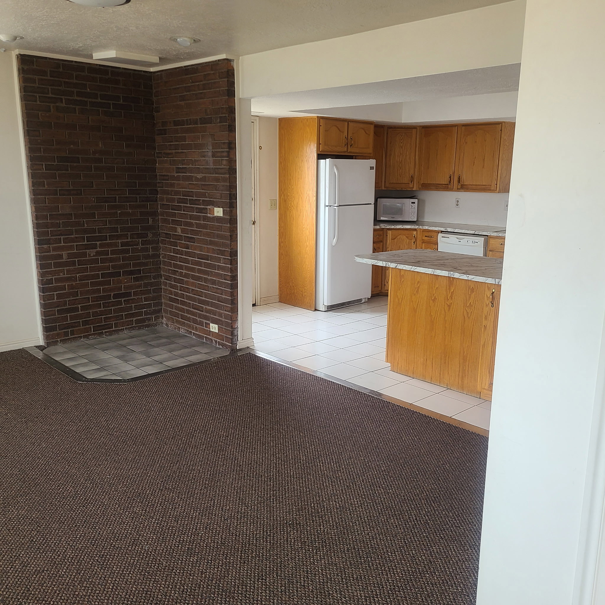 Kitchen featuring white appliances, light countertops, wood finish cabinetry, light colored carpet, and light tile patterned flooring