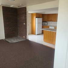 Kitchen featuring white appliances, light countertops, wood finish cabinetry, light colored carpet, and light tile patterned flooring