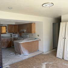 Kitchen with a peninsula, wood finish cabinetry, light countertops, a textured ceiling, and white appliances