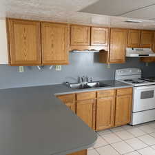Kitchen with white electric stove, wood finish cabinets, light tile patterned flooring, light countertops, and a textured ceiling