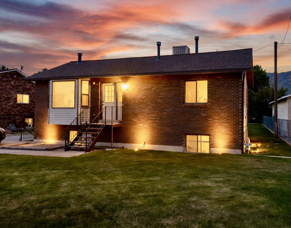 Back of house at dusk featuring a lawn, brick siding, and a shingled roof
