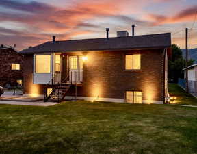 Back of house at dusk featuring a lawn, brick siding, and a shingled roof