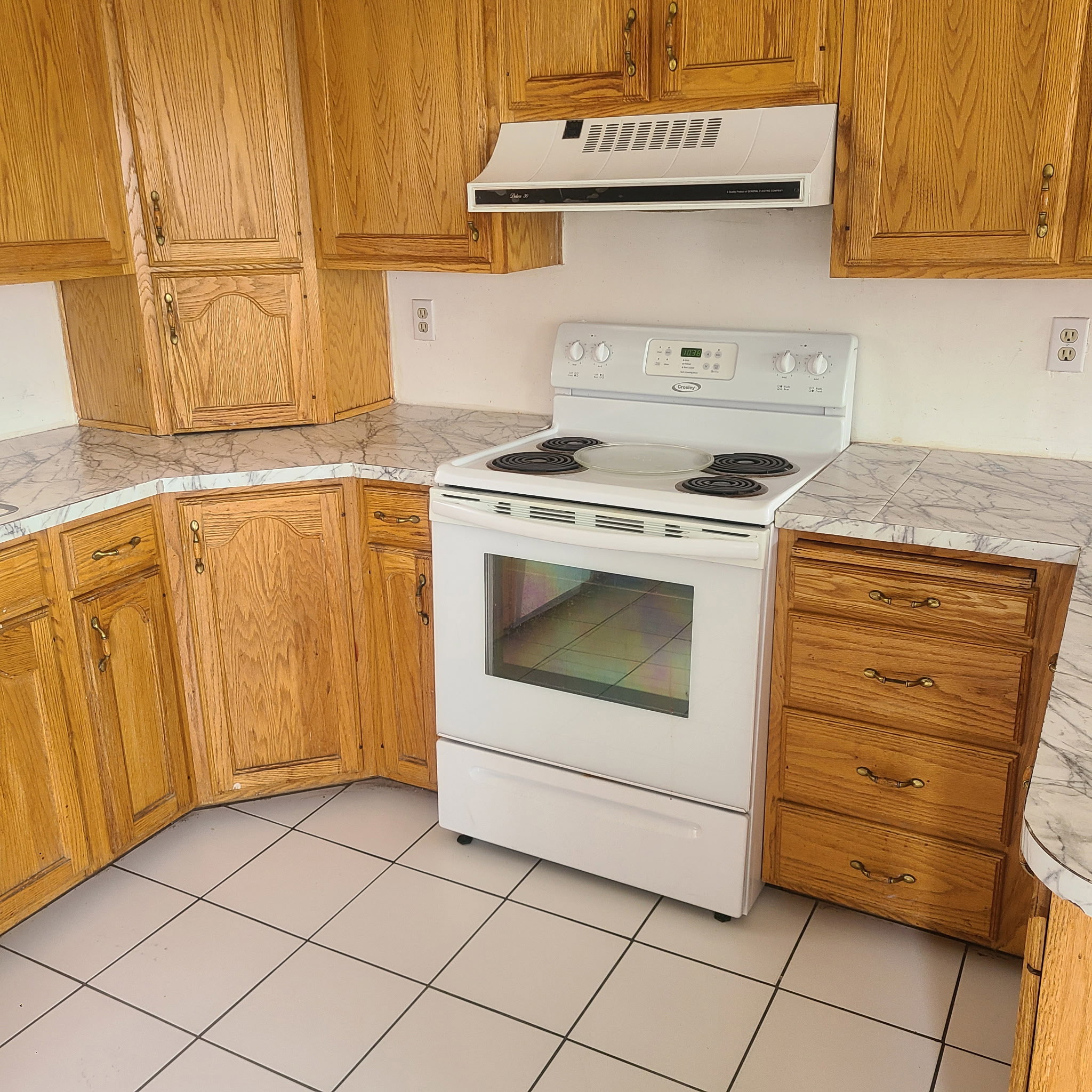 Kitchen with white electric range oven, range hood, wood finish cabinetry, and light tile patterned floors