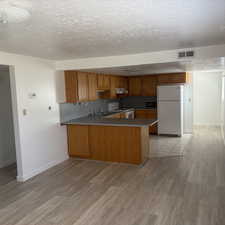 Kitchen with wood finish cabinetry, a peninsula, white appliances, a textured ceiling, and light wood-style flooring