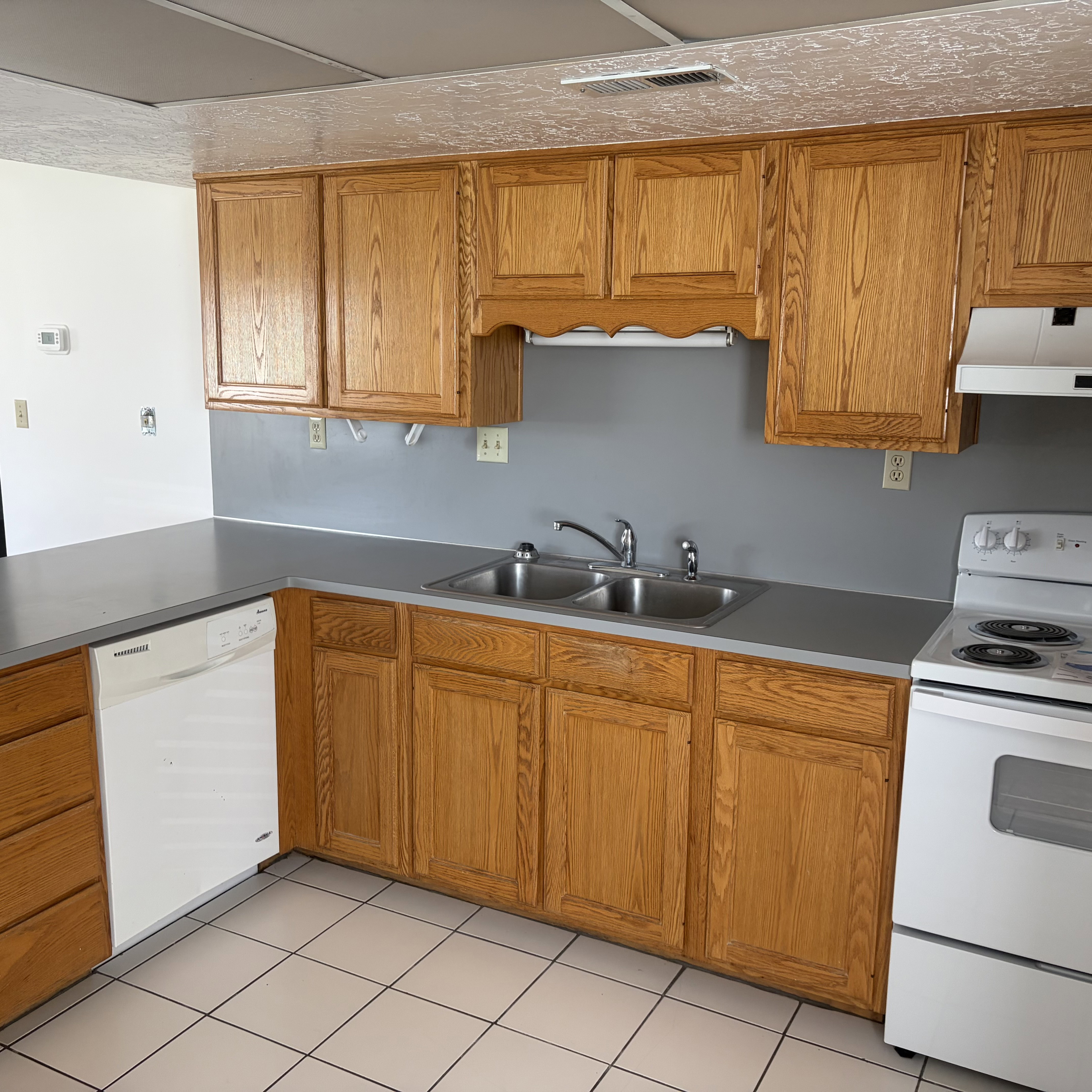Kitchen with white appliances, wood finish cabinets, light tile patterned floors, and light countertops