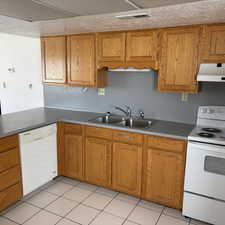 Kitchen with white appliances, wood finish cabinets, light tile patterned floors, and light countertops