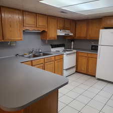 Kitchen with wood finish cabinets, white appliances, light tile patterned floors, a peninsula, and a textured ceiling