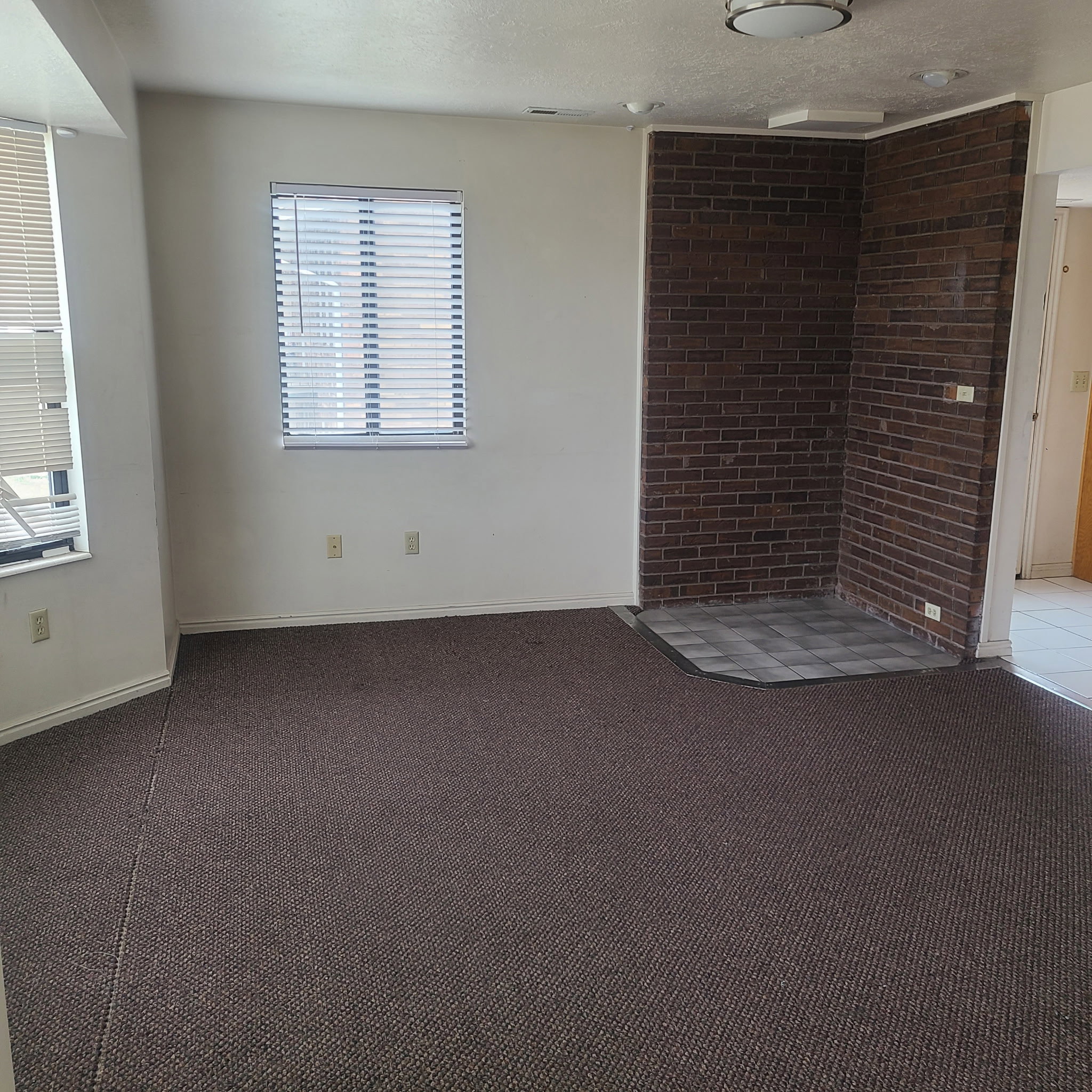 Unfurnished room with dark colored carpet, a textured ceiling, and brick wall