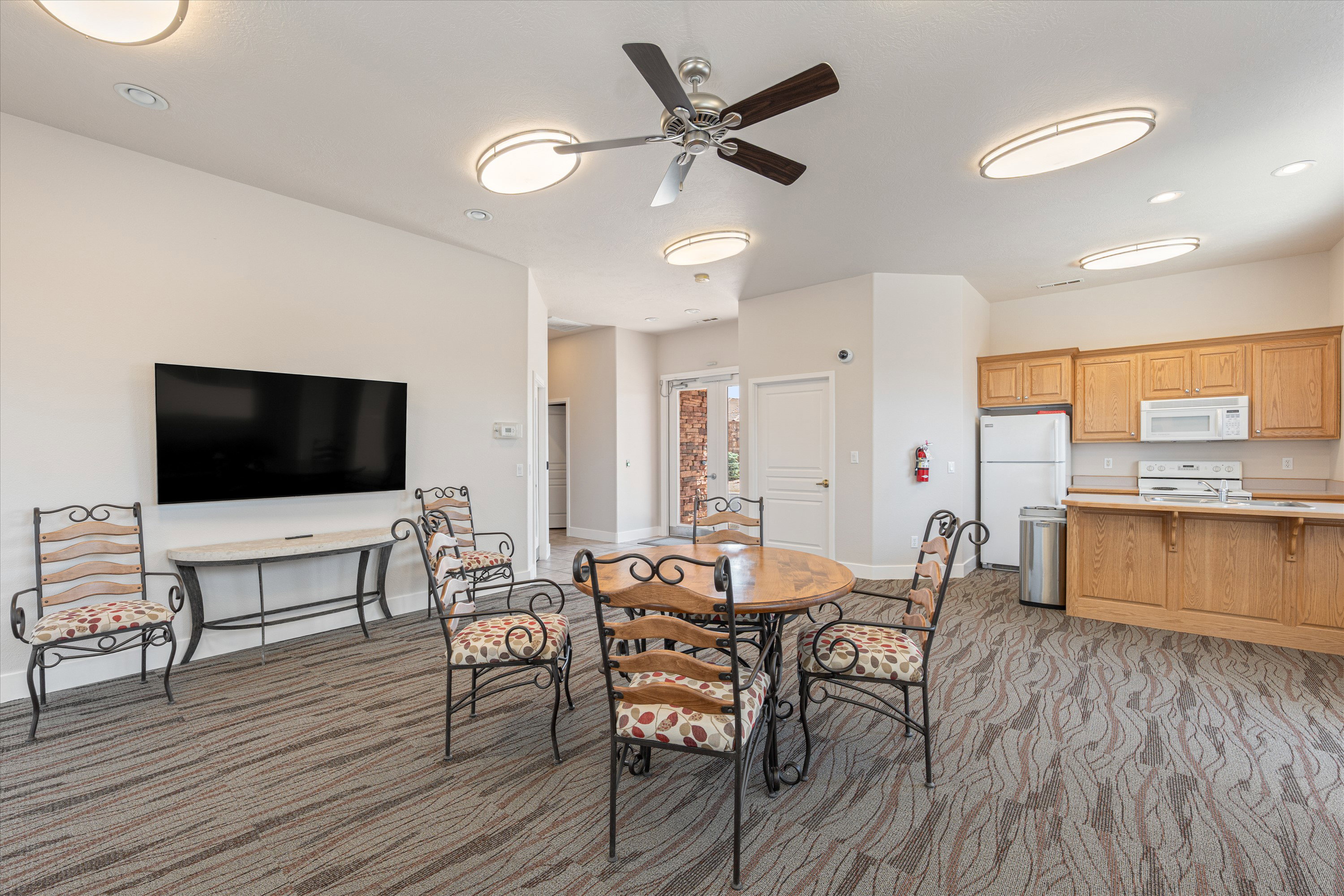 Spacious common area featuring patterned carpeting, recessed lighting, ceiling fan, and a functional kitchen space with wood cabinetry and white appliances