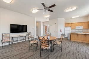 Spacious common area featuring patterned carpeting, recessed lighting, ceiling fan, and a functional kitchen space with wood cabinetry and white appliances