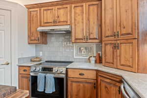 Kitchen with stainless steel appliances, light stone countertops, wood finish cabinetry, and backsplash