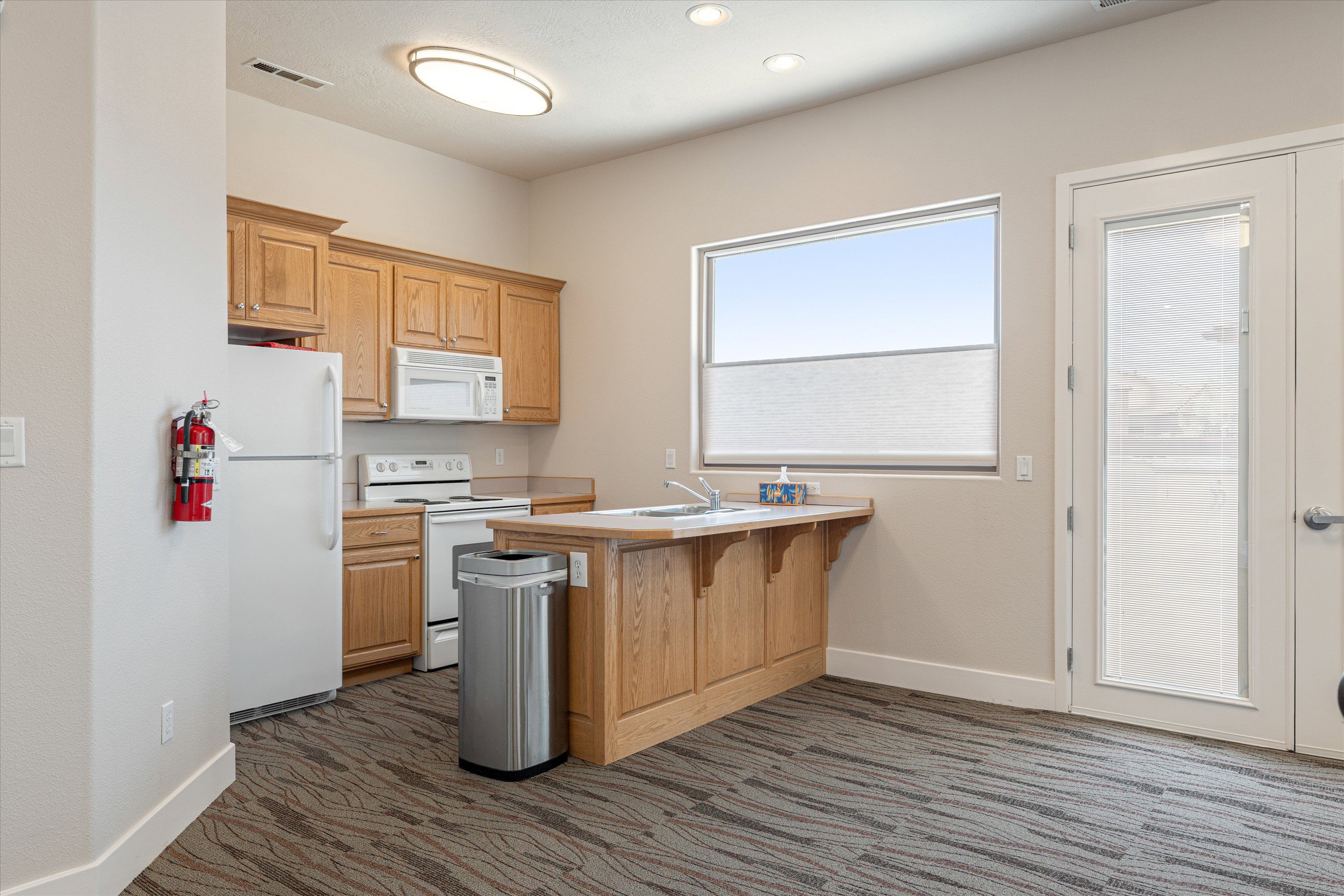 Kitchenette featuring wood cabinetry, white appliances, a built-in sink, and a large window