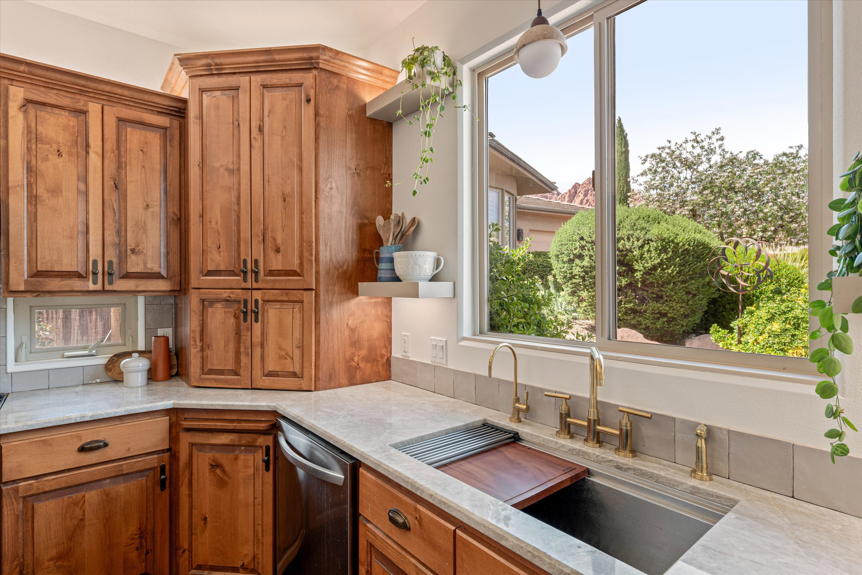 Kitchen featuring wood finish cabinetry, light stone countertops, open shelves, stainless steel dishwasher, and hanging light fixtures