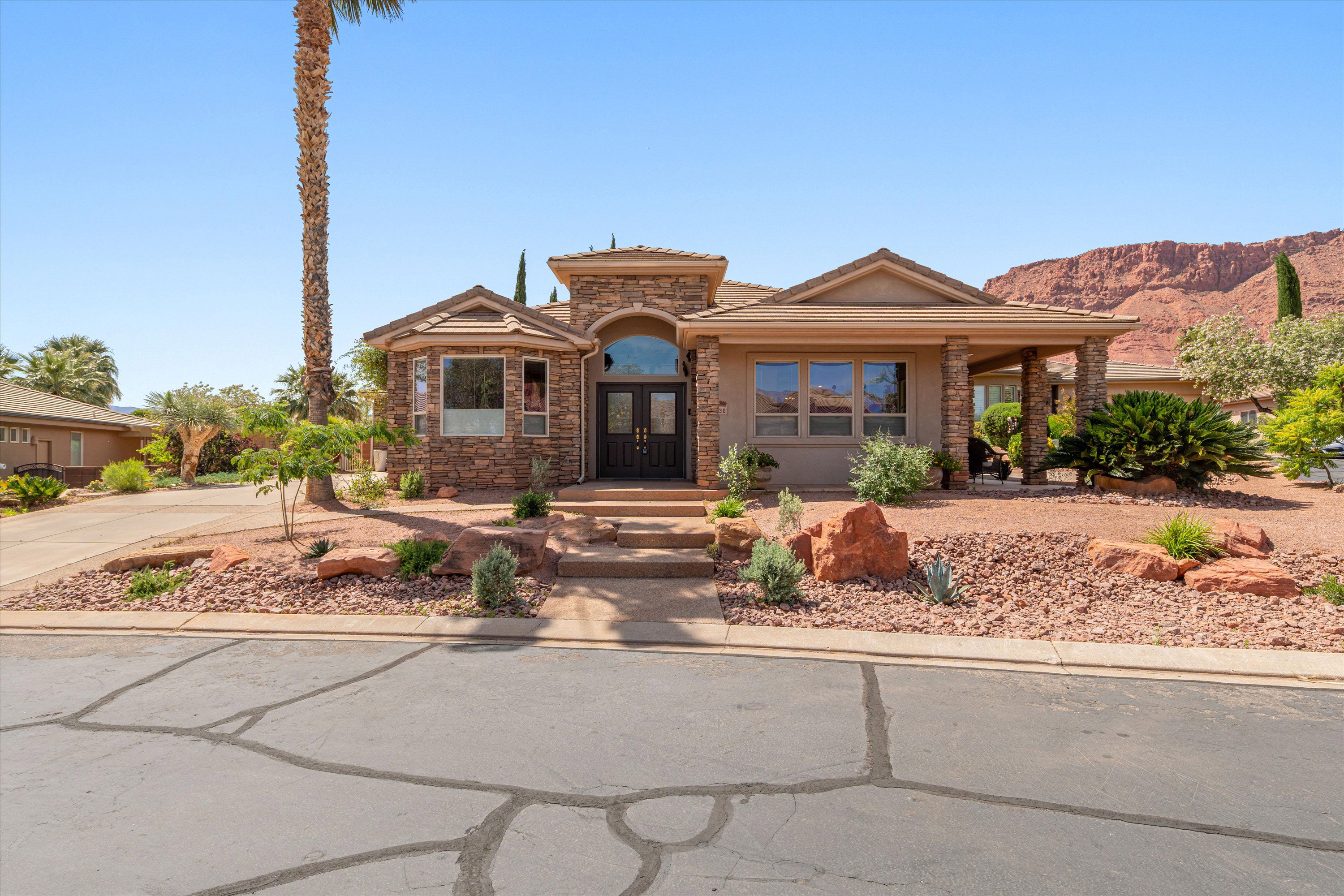 View of front facade with stone siding, french doors, a tile roof, covered porch, and stucco siding