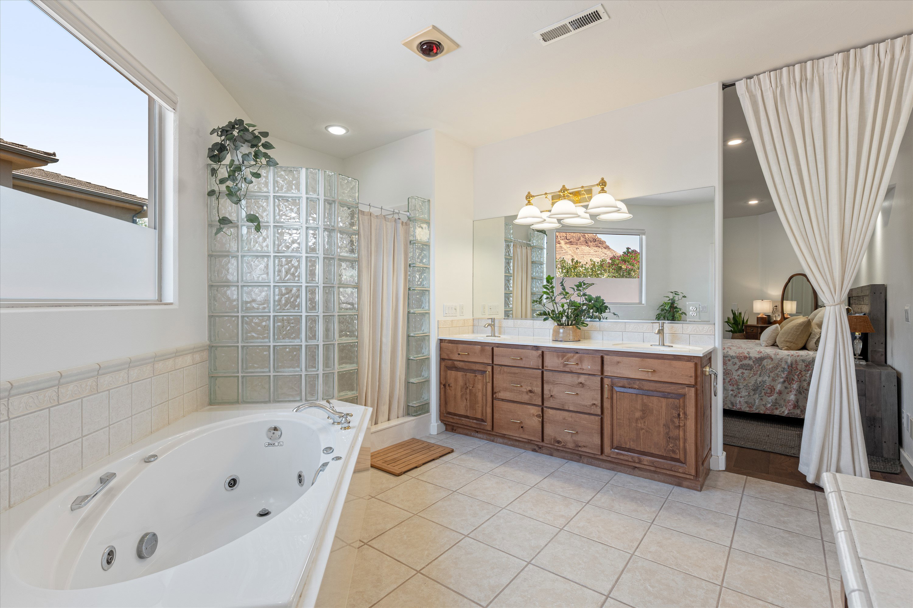 Spacious bathroom featuring a built-in jetted tub, glass block shower enclosure, wood-finish double vanity with undermount sinks, and tile flooring