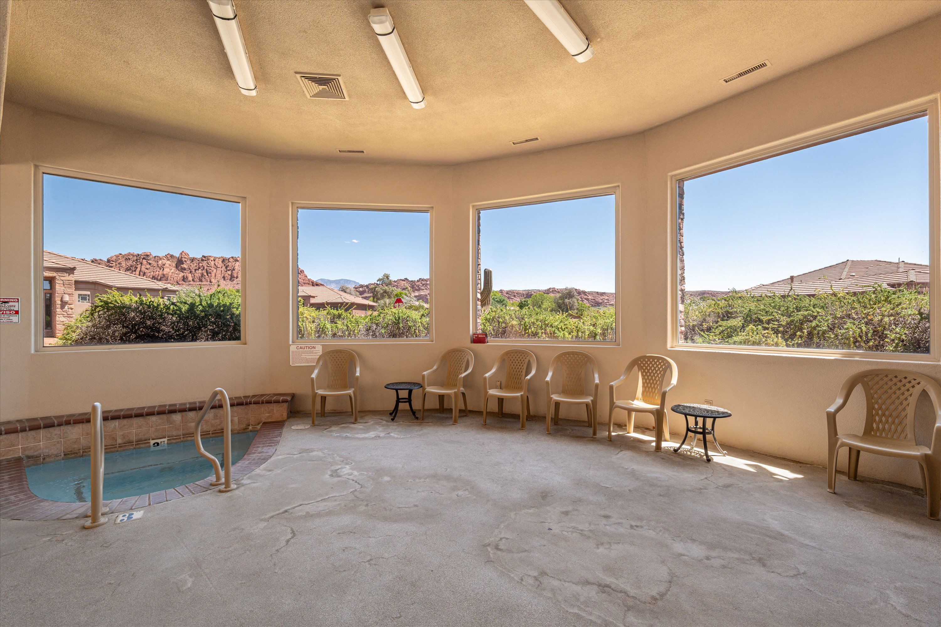 Indoor spa featuring a tiled surround, grab rails, and multiple expansive windows showcasing distant red rock formations and surrounding greenery