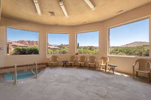 Indoor spa featuring a tiled surround, grab rails, and multiple expansive windows showcasing distant red rock formations and surrounding greenery