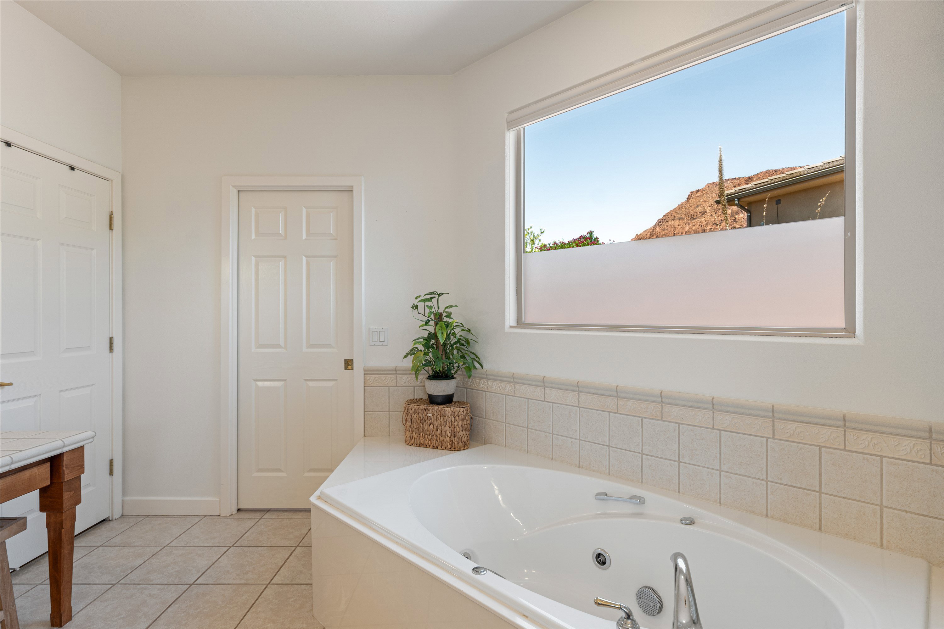 Corner soaking tub with deck-mounted fixtures, set against a tiled surround and a large horizontal window