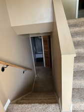 Carpeted staircase with a wood handrail featuring black metal brackets