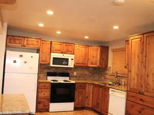 Kitchen with white appliances, light stone counters, wood finish cabinets, decorative backsplash, and recessed lighting