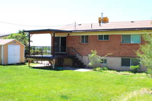 Back of property featuring a deck, a 2nd storage unit, a yard, brick siding, and a shingled roof