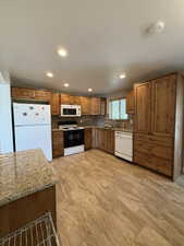Kitchen featuring wood cabinetry, stone-finish countertops, and a full suite of white appliances