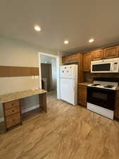 Kitchen area featuring wood cabinetry, white appliances, and a built-in desk with a stone-finish countertop