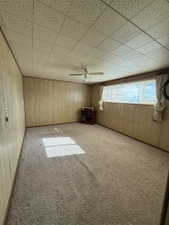 Spacious room featuring paneled walls, a ceiling fan, and carpeted flooring