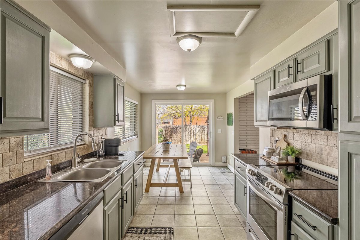 Kitchen featuring tasteful backsplash, stainless steel appliances, light tile patterned floors, dark stone countertops, and gray cabinetry