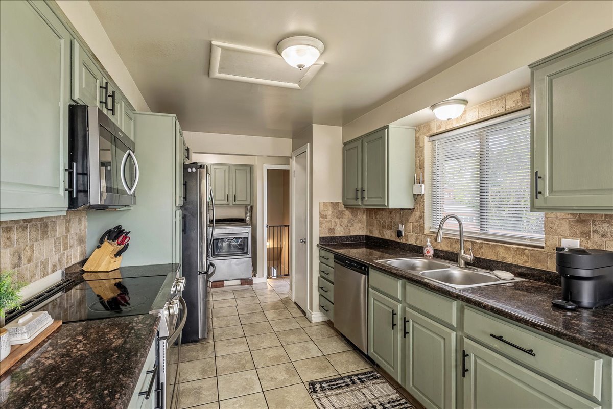 Kitchen with green cabinets, decorative backsplash, and stainless steel appliances