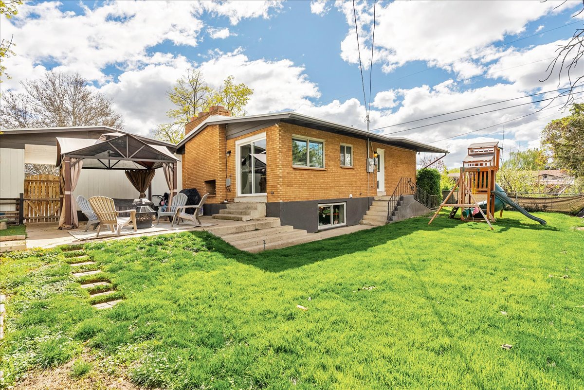 Back of house with entry steps, brick siding, a playground, a chimney, and a patio area