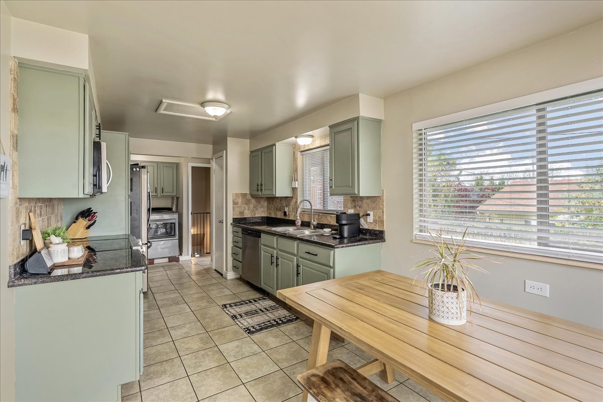 Kitchen featuring green cabinets, dark stone countertops, light tile patterned floors, and stainless steel appliances