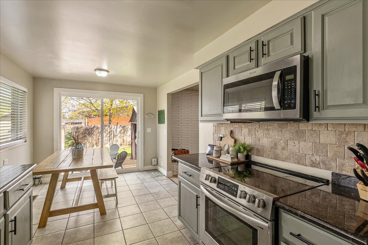 Kitchen with stainless steel appliances, light tile patterned flooring, gray cabinets, backsplash, and dark stone countertops