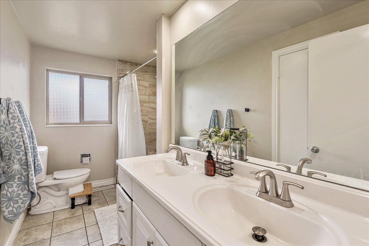 Full bathroom featuring double vanity, light tile patterned floors, and a shower with shower curtain